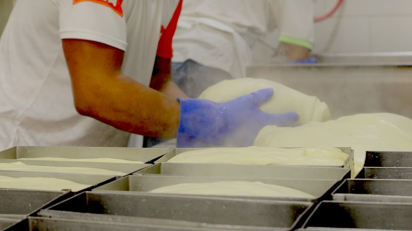 Manos con guantes colocan mozzarella recién hecha en moldes de acero en la planta